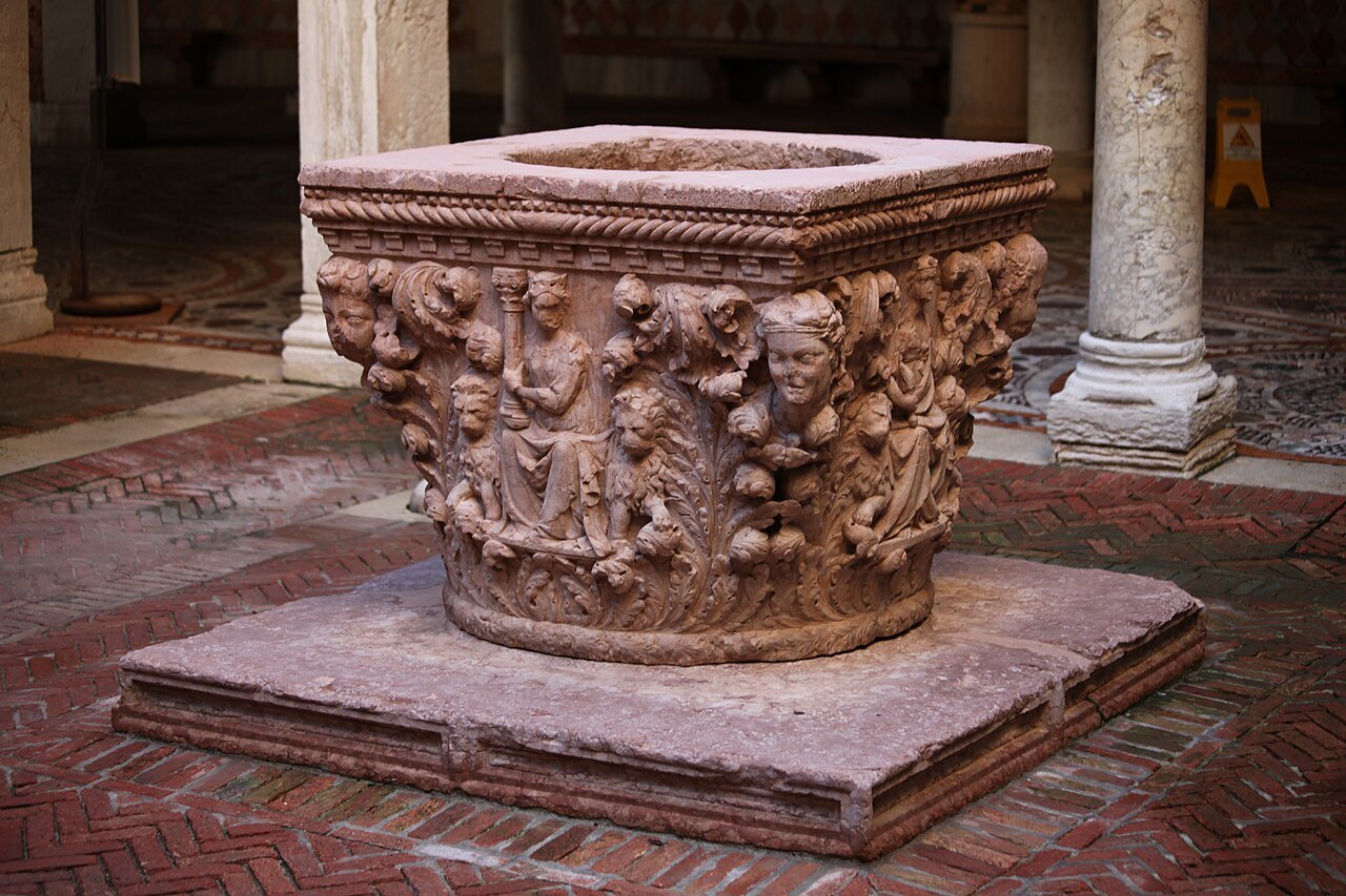 A Renaissance wellhead carved with figures in a courtyard