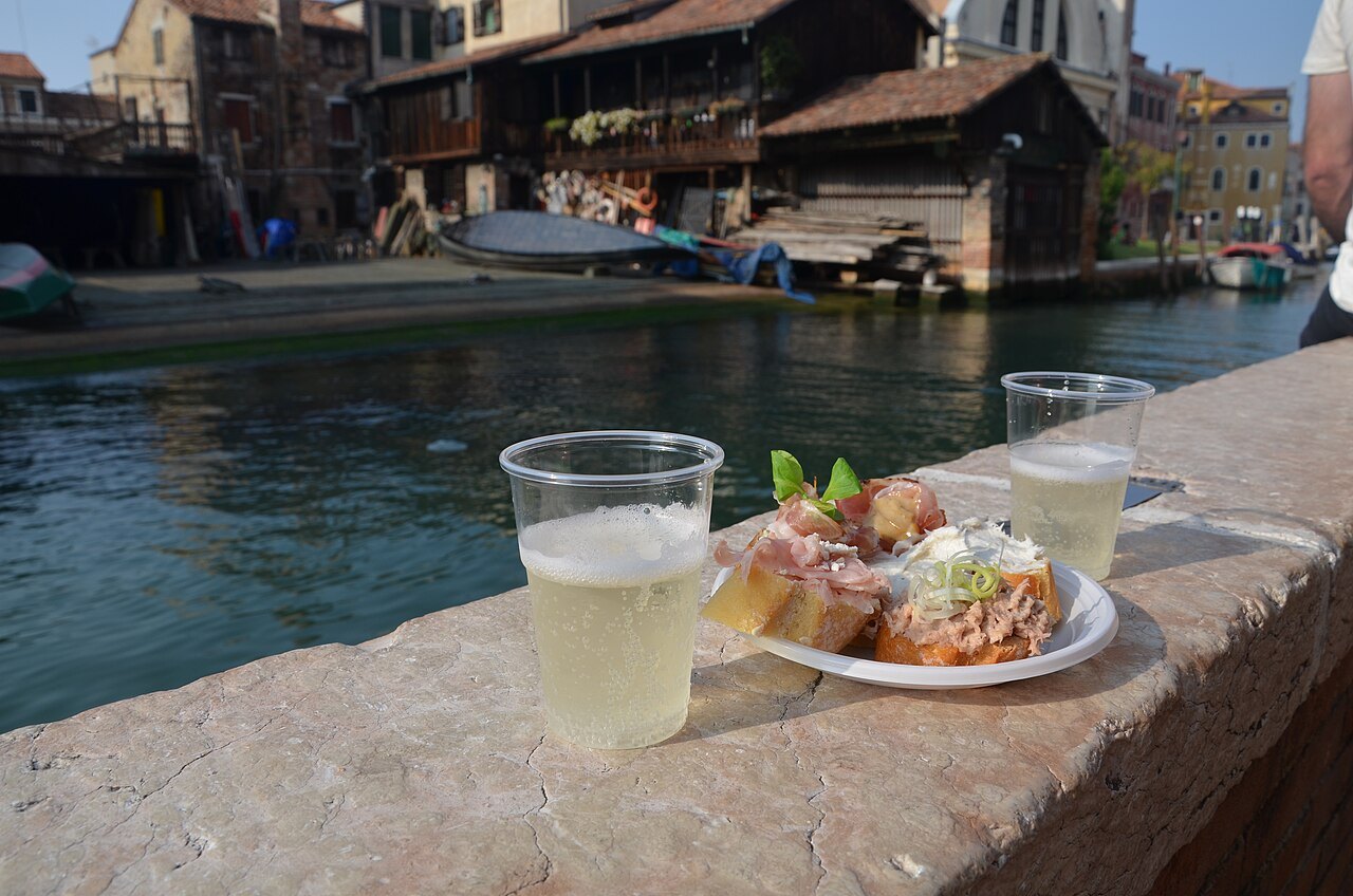 A glass of Prosecco and cicchetti on a canal wall