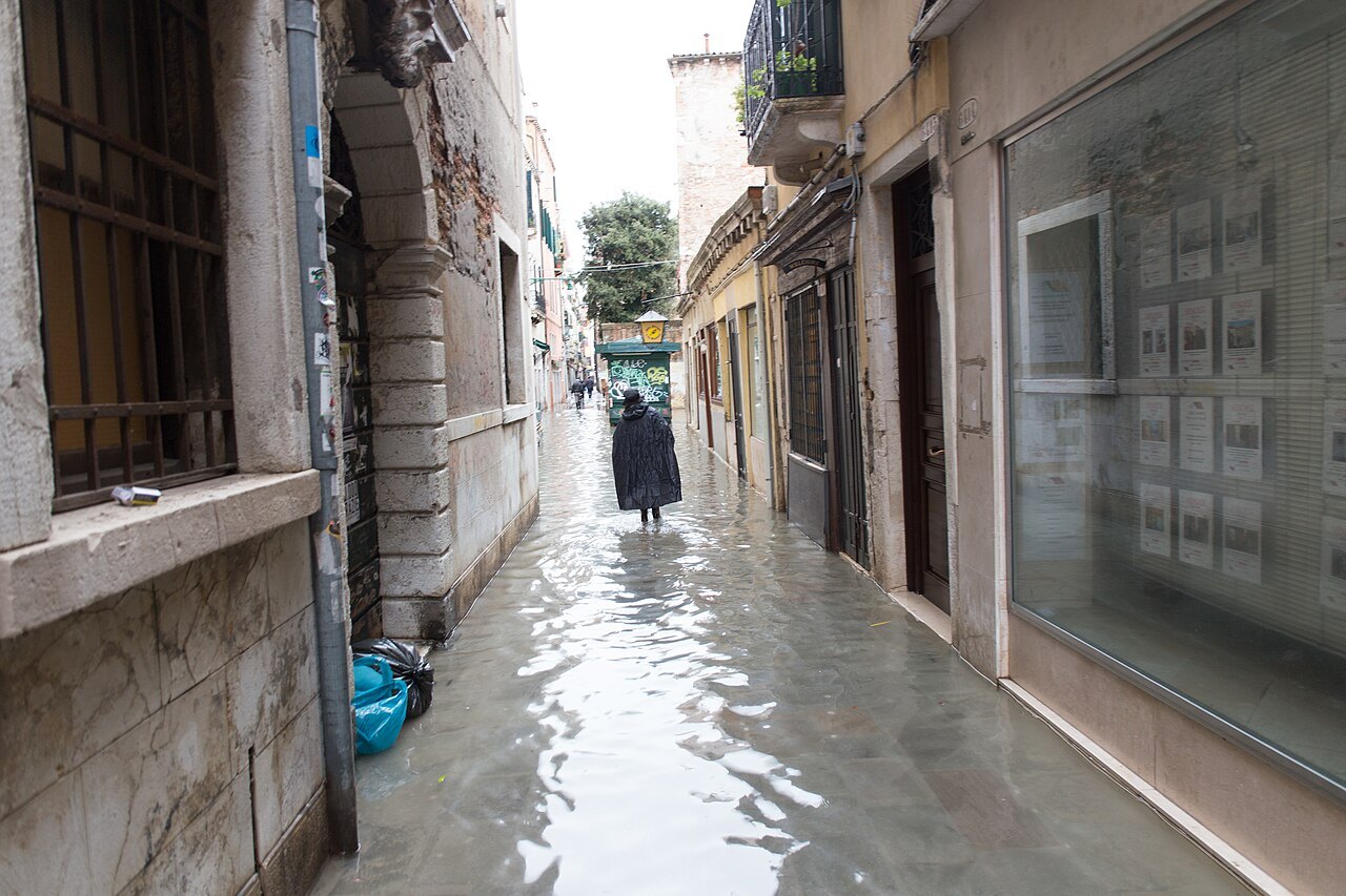A woman walking through high water in a narrow calle