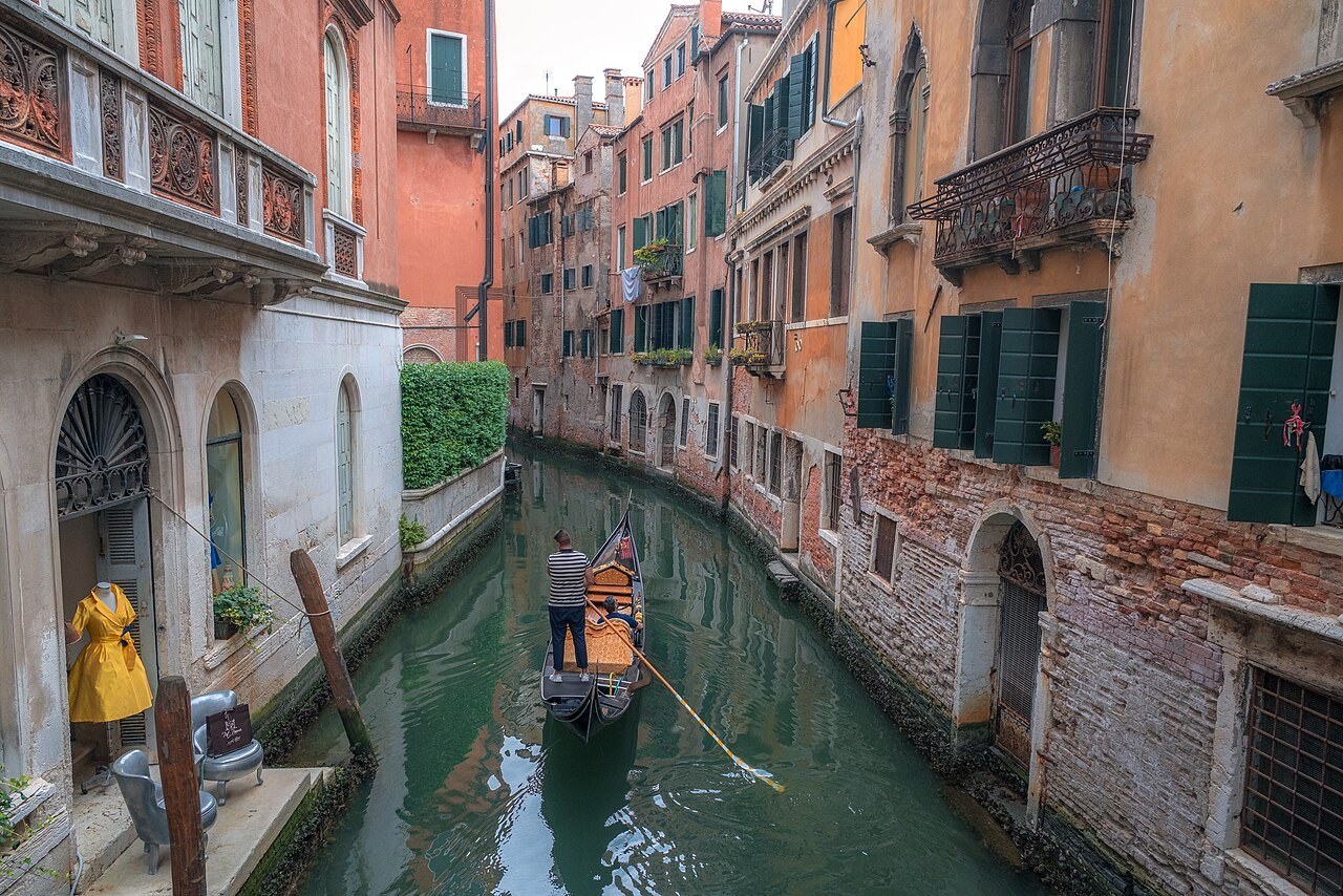 A gondolier in a narrow canal between tall houses