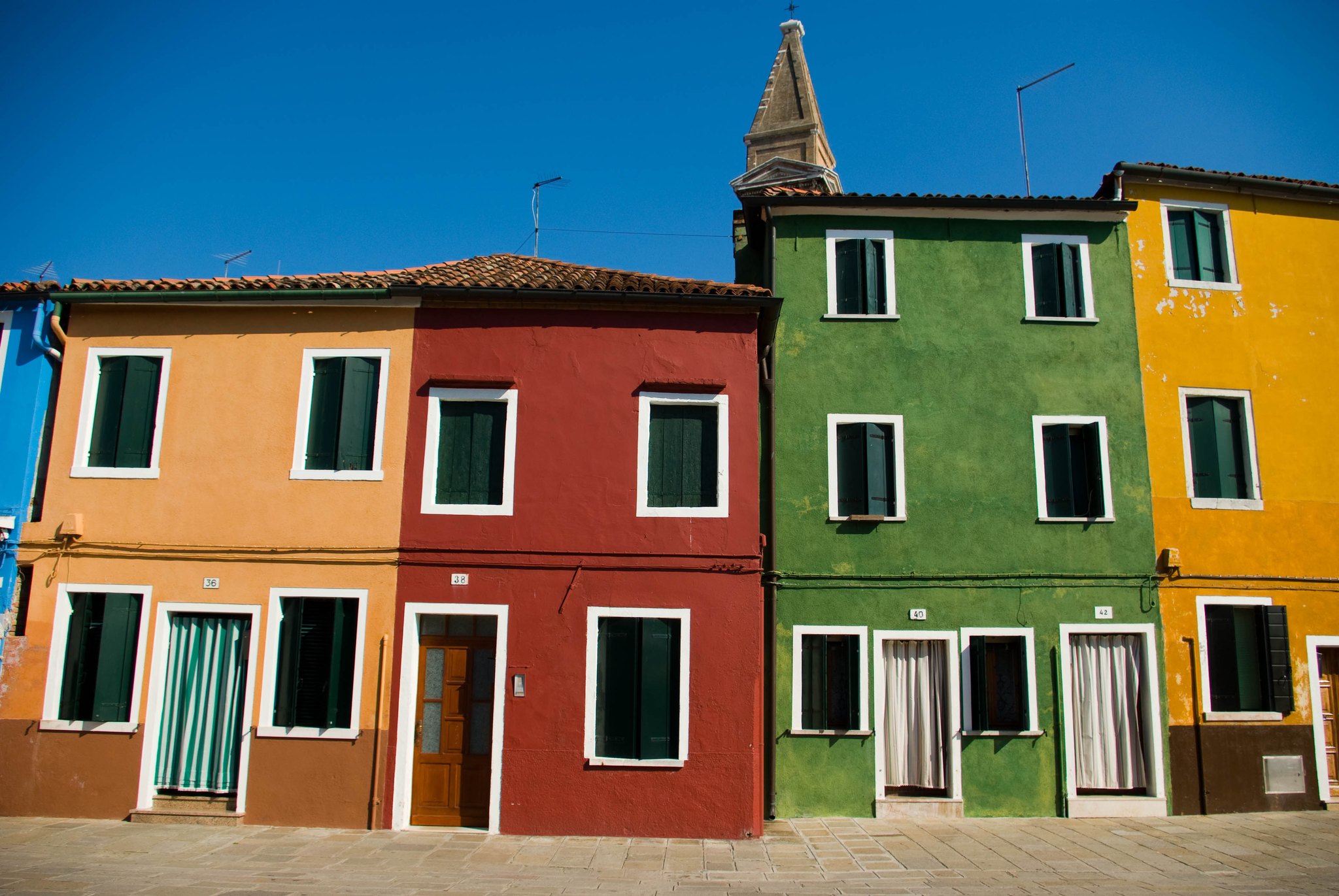 Four Burano houses side by side in orange, green, blue and yellow with white window frames
