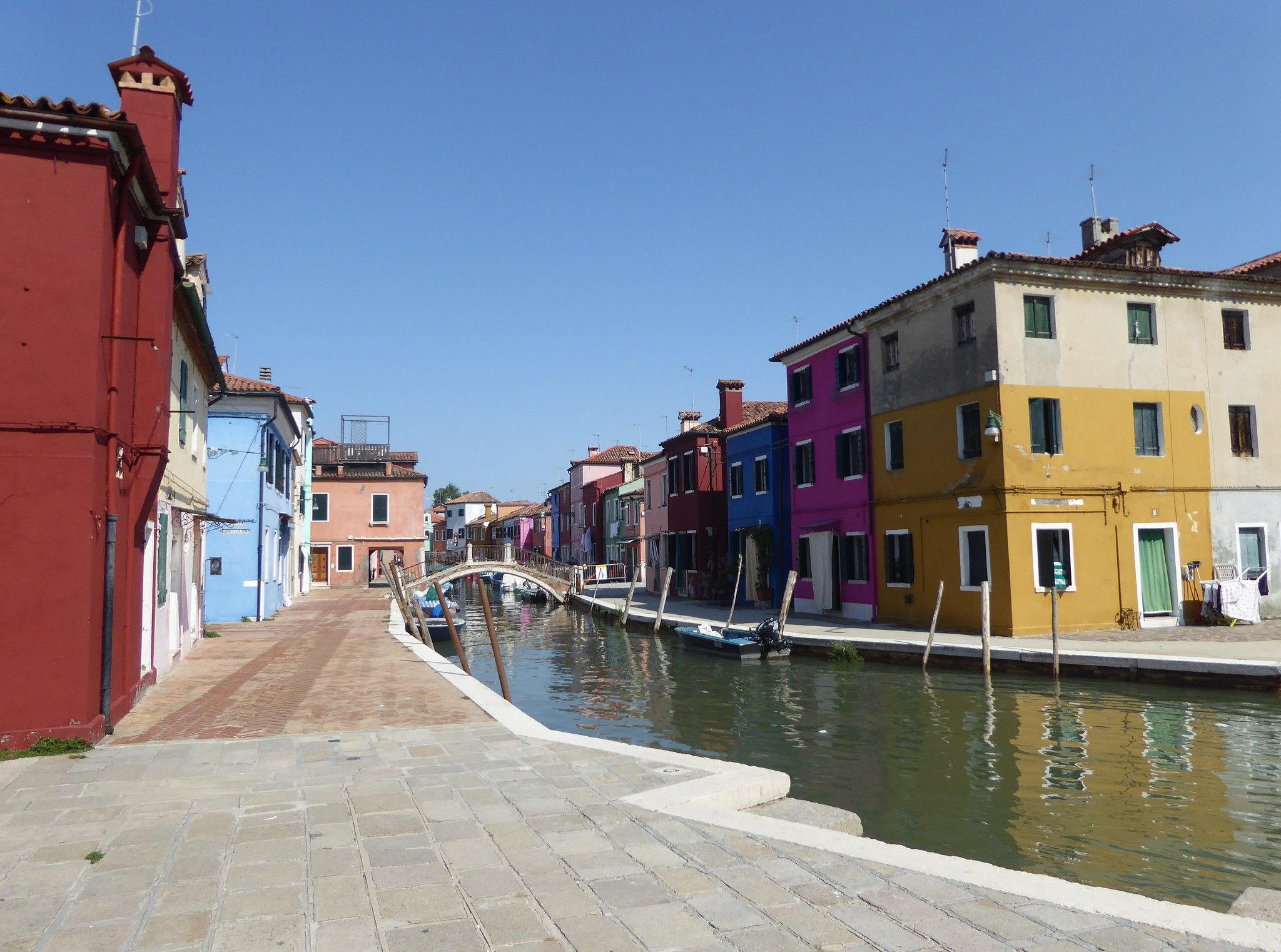 A canal in Burano seen from the paving, a red house at the corner and coloured fronts running away