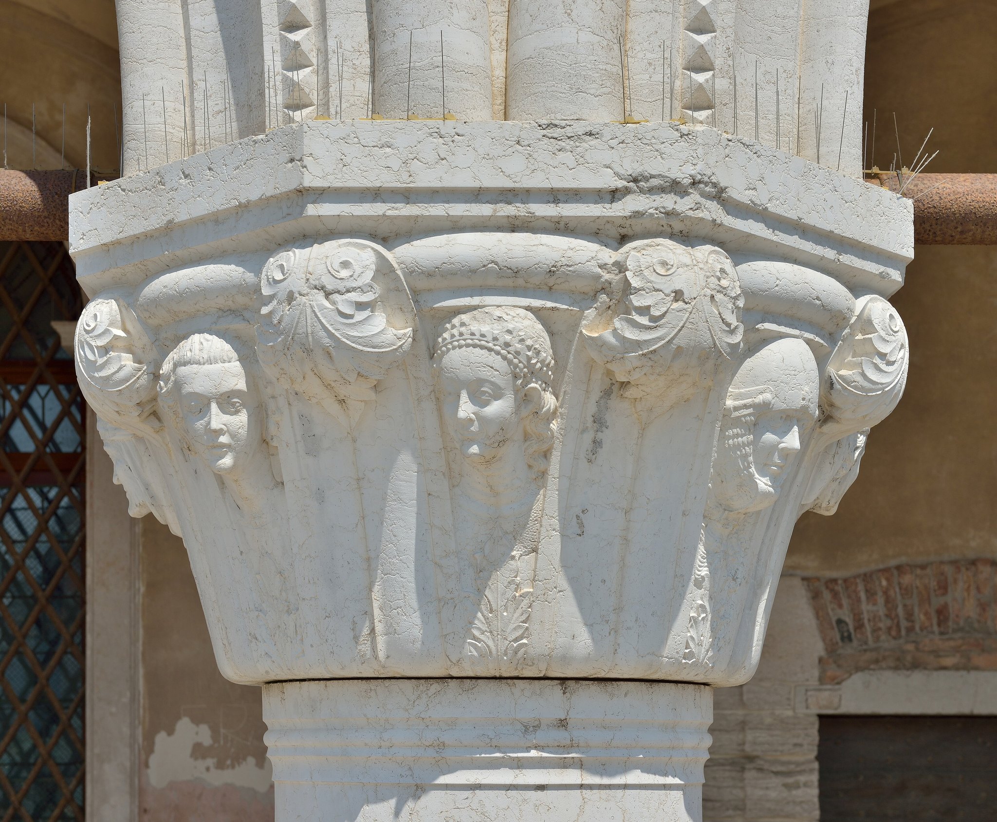 A carved capital on the Doge's Palace arcade, a ring of heads under the stonework
