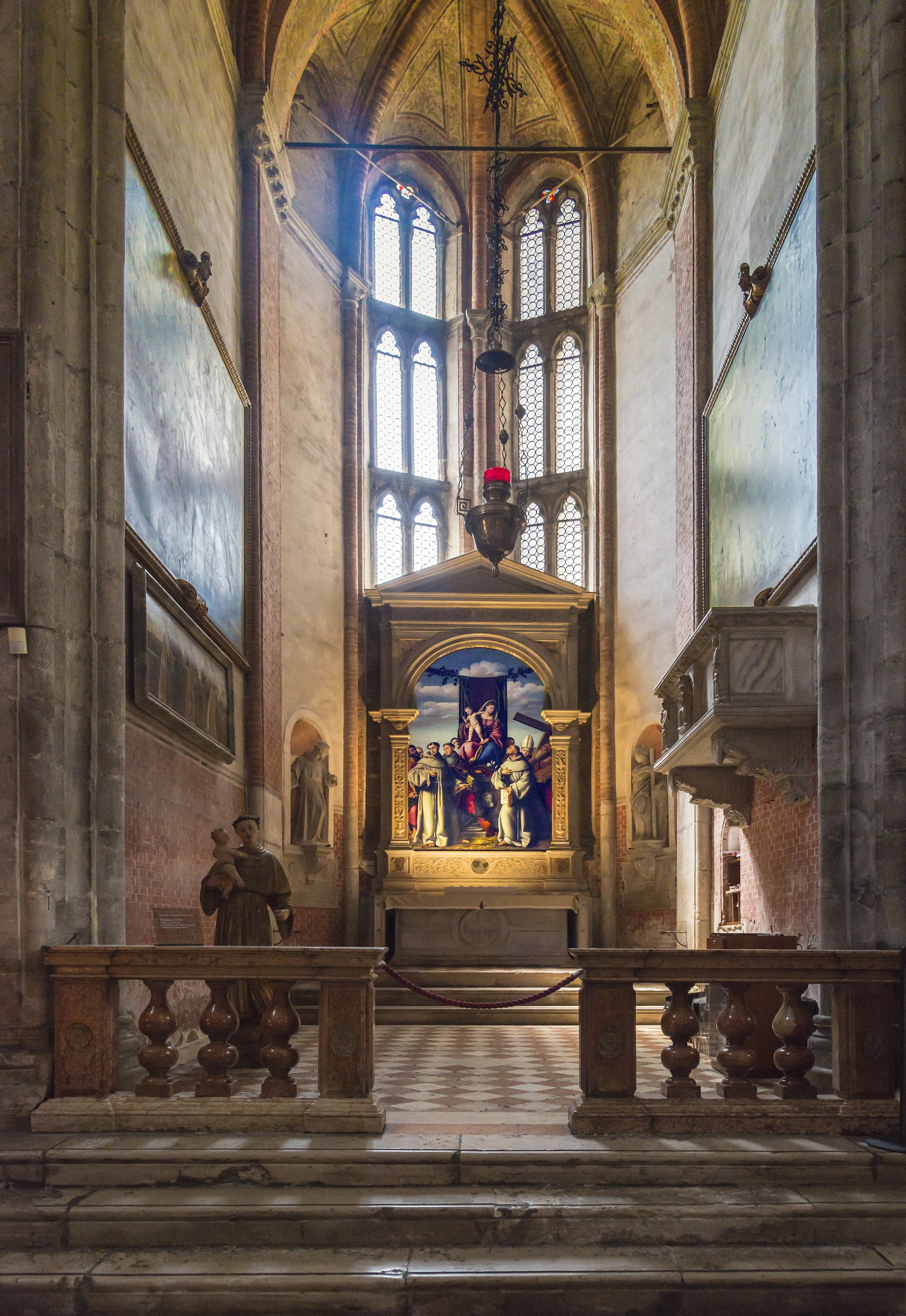 A side chapel in the Frari, an altarpiece glowing at the end of a dim brick nave