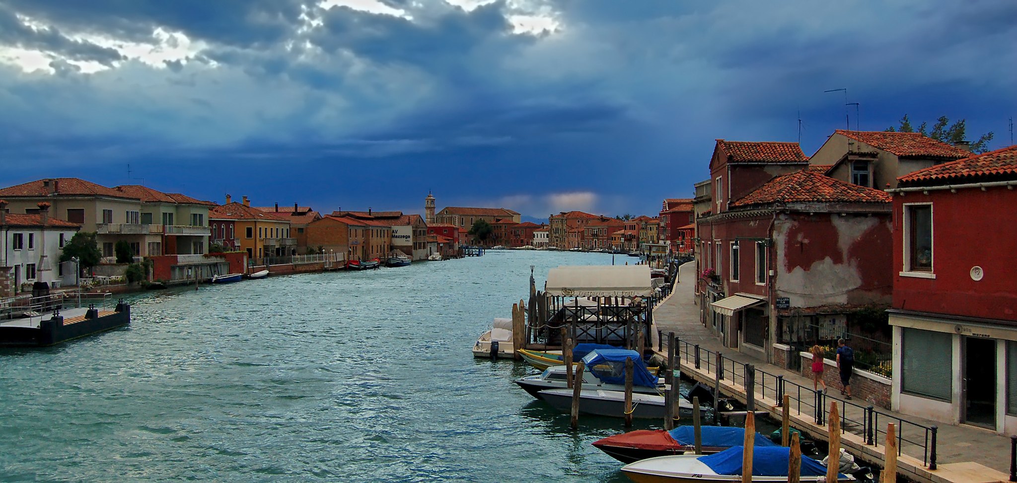 A canal on Murano lined with low houses and moored boats, wider and quieter than anything in Venice itself