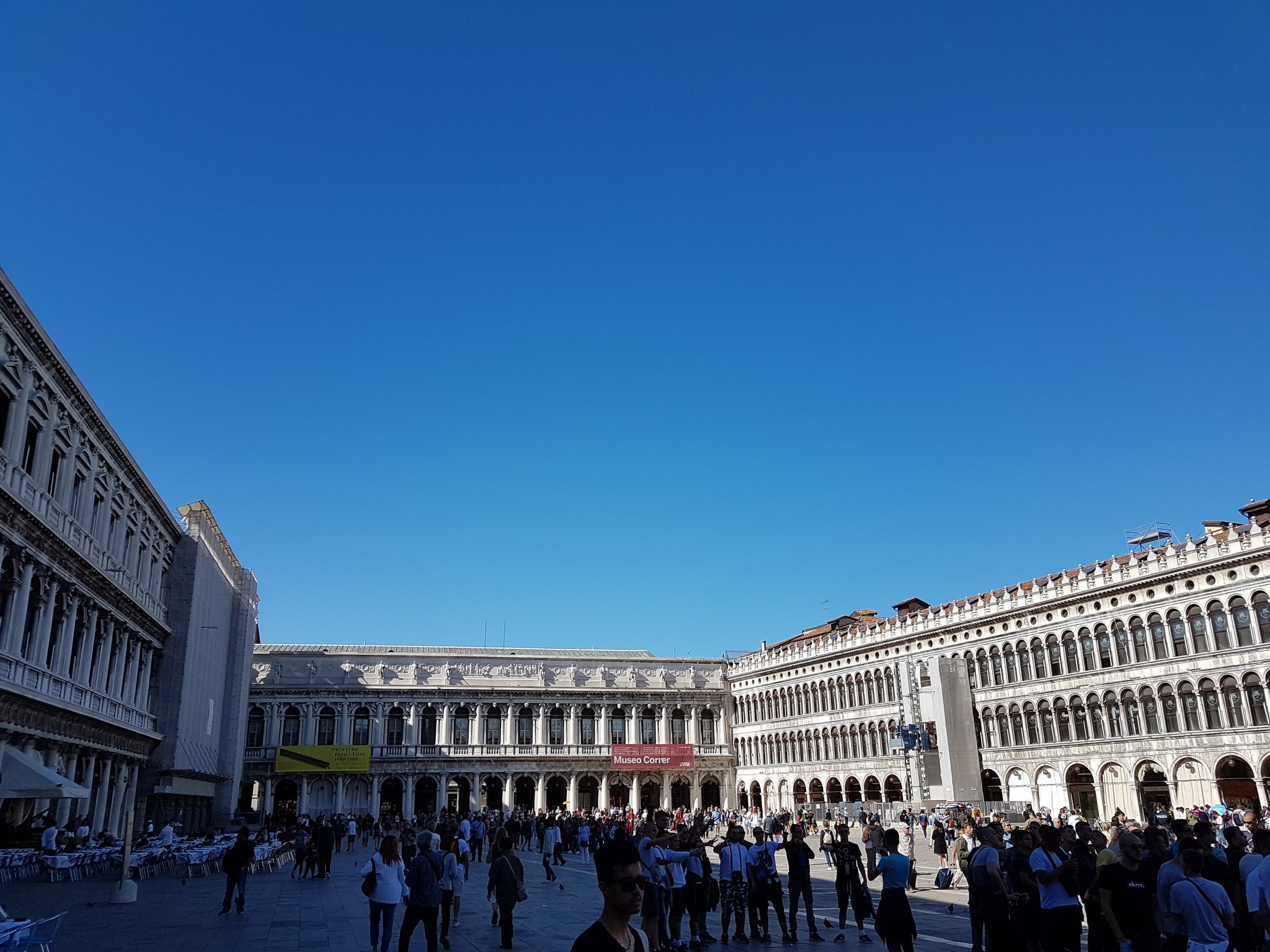 Piazza San Marco on a clear day, the long arcades of the Procuratie running down both sides above the crowd
