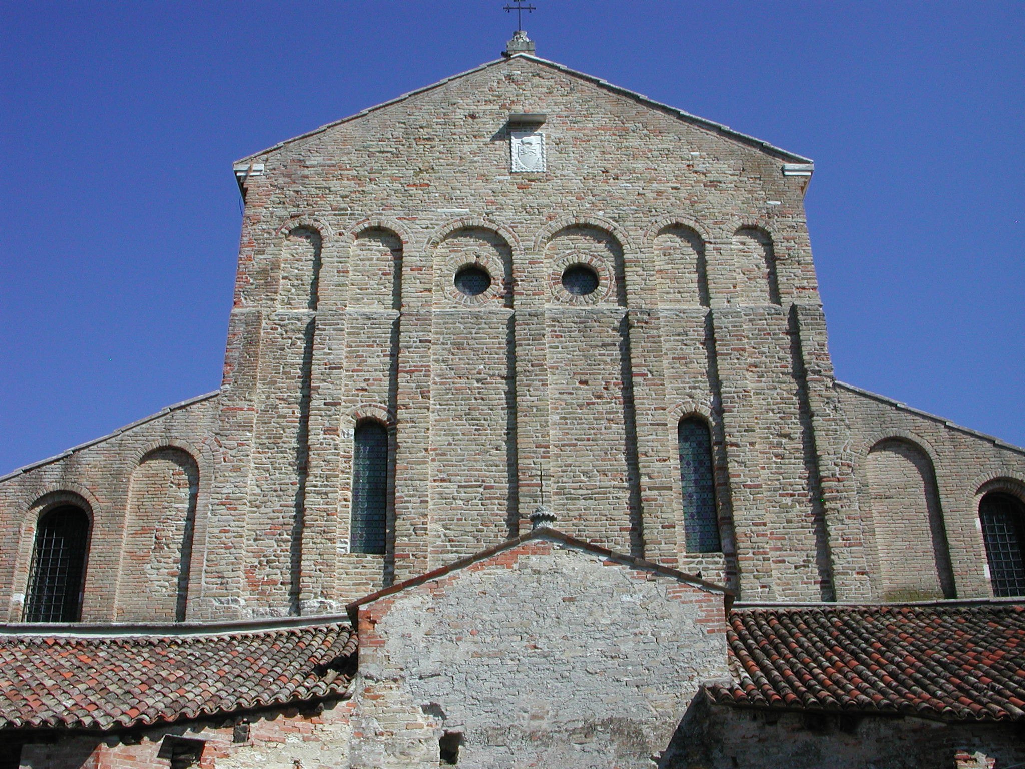 The front of Torcello's cathedral, plain brick under a low roof with the campanile beside it