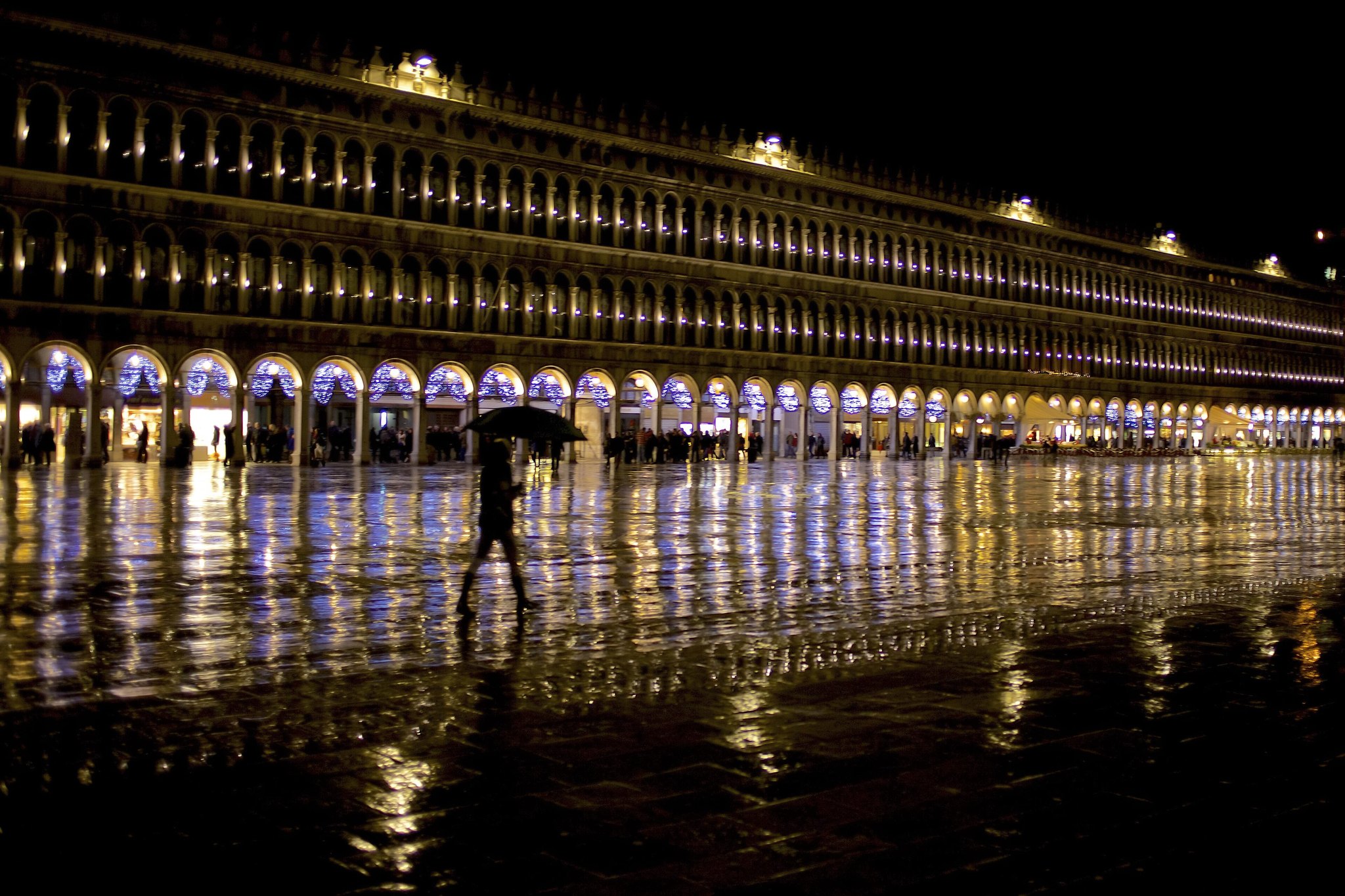 Raised walkways laid across a flooded square during acqua alta, with people crossing on them